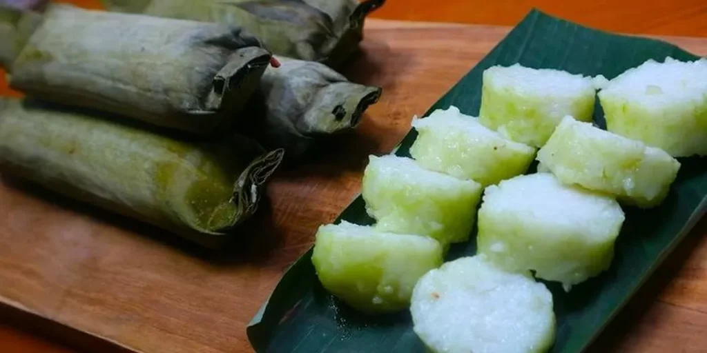 Potongan lontong yang sangat padat, halus, dan berwarna hijau zaitun di atas daun pisang.